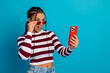 © deagreez - Young stylish woman smiles at her phone wearing a striped top and red sunglass against a bright blue background