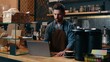 © Yuliia - Pensive Caucasian staff employee restaurant worker barista guy using laptop ordering products online shopping in Internet male small business owner thinking in cafeteria waiter man type computer cafe