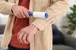 © New Africa - Man cleaning shirt with lint roller at home, closeup