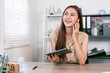 © NAMPIX - Happy Asian businesswoman talking on a video call with wireless earbuds while holding a digital tablet in her office.
