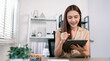 © NAMPIX - Smiling young Asian professional woman working with a digital tablet and stylus pen in a modern home office.