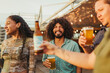 © STOCKEROcr - Friends enjoy a light-hearted moment at a rooftop gathering, holding bottles and glasses of beer while sharing smiles and laughter.