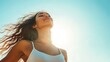 © pariimage - horizontal portrait of fit woman basking in sunlight arms slightly raised face tilted upwards wind blowing hair serene expression clear sky as backdrop summer vitality and freedom