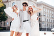 © halayalex - Young three stylish friends posing in the street. Fashion man and two cute female dressed in casual summer clothes. Smiling models having fun. Cheerful women and guy outdoors, in sunny day, sunglasses
