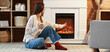 © Pixel-Shot - Young woman with cup of cocoa sitting near fireplace at home in evening