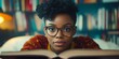 © Ilja - A young African American woman wearing glasses enjoys reading a book in a cozy indoor setting.
