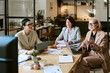 © AnnaStills - Three middle aged Caucasian women sitting at table discussing business strategy, using laptop and digital tablet, taking notes during professional meeting in modern office workspace