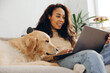 © Maria Vitkovska - Candid African American woman businesswoman using working on laptop petting golden retriever