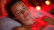 © Maksym - Woman rests peacefully under red light therapy, soft crimson illumination enveloping her face and body, serene spa atmosphere filled with a warm healing glow and calm reflections