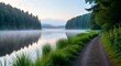 © SarghiArts - Tranquil morning mist hovers over a serene lake, reflecting the lush green trees and a gentle path winding along the grassy shore during the golden hour, creating a peaceful natural landscape
