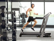 © Ljupco Smokovski - Full length shot of a man running on a treadmill at a gym and listening to music