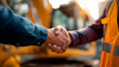 © Катерина Євтехова - Construction worker shaking hands with foreman on site tight crop on hands vests and hardhats partially in frame machinery bokeh workplace agreement faceless no visible faces