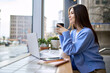 © insta_photos - Happy calm lady student enjoying warm hot drink with mug in hands working or studying online. Young smiling woman sitting holding cup drinking tea or coffee relaxing in cafe looking through window