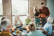 © deagreez - Family gathers for a festive Thanksgiving feast as a couple presents a roasted turkey to delighted seniors and grandchildren in a warm brick dining room