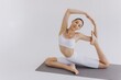 © anatoliycherkas - Beautiful slim young woman in white sportswear doing exercises and stretching, practicing yoga isolated on white background