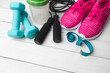 © O.Farion - Pink sneakers, blue dumbbells, jump rope, water bottle, shaker and measuring tape on white wooden background with copy space, fitness equipment and active lifestyle concept