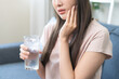 © KMPZZZ - Suffering from toothache, hurt asian young woman touch cheek, face expression ache or feel pain, sensitive molar teeth, hand holding glass of water with ice, inflammation when drink cold, healthcare.
