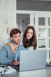 © Daniel - A smiling woman stands behind her partner as he works on a laptop at home. Their teamwork and shared focus reflect motivation, love, and the balance of modern relationship goals.