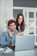 © Daniel - A smiling woman stands behind her partner as he works on a laptop at home. Their teamwork and shared focus reflect motivation, love, and the balance of modern relationship goals.