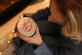 Woman enjoying cocoa drink with whipped cream and sprinkles near fireplace at home, above view