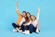 © Anastasiya - Happy family sitting together on floor in studio, raising arms and smiling. Blue background, concept of joy, success, and positive family lifestyle