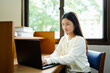 © Stella 16 - Young Asian woman studying in a library using a laptop and book. Ideal for concepts like education, learning, focus, university