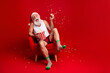 © deagreez - Santa enjoys popcorn on Christmas Eve relaxing in a red chair wearing hat striped socks and smiling