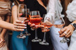 © shchus - A close-up photo of women's hands holding glasses of alcoholic cocktails at a bachelorette party. Concept of female friendship.