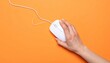 © aulia - A Person's Hand Maneuvering a White Computer Mouse on a Vibrant Orange Surface