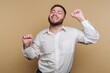 © bodnarphoto - A joyful man in a white shirt dancing against a beige background.