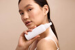 © SHOTPRIME STUDIO - asian woman is photographed in a soft studio as she holds a white bottle near her face, showcasing a skincare moment with a calm, focused expression and gentle lighting.