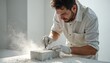 © Maryna - Man carves marble block with chisel in white studio. Artist wears gloves, dust flies. Skilled artisan crafts sculpture with precise movements, focused on creative work.
