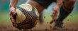 © Maryna - Rugby player grips muddy ball firmly with dirty hand on wet ground. Athlete prepares for intense game action, ready to play hard on field. Sport player shows strength and fierce determination needed.