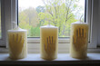© Alex & M Studio - Three large white Halloween candles with handprint impressions, sitting on a window sill overlooking a green spring garden. Concept of homemade crafts, memory, or a unique decorative item