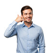 © SimpleDesignStudio - Smiling young adult Caucasian man in a blue shirt making a 'call me' gesture, looking happy and friendly on a transparent background.