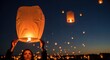 © Nina - Young woman holding a glowing paper sky lantern at dusk, preparing to release it into the dark night sky filled with many other floating illuminated lanterns.