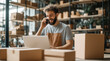 © D.APIWAT - Cheerful small business owner multitasking with phone call and laptop amidst shipping boxes in modern e-commerce warehouse for efficient order fulfillment and customer service.