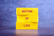 © Garik - Three bright yellow blocks are stacked, each bearing part of a phrase. The message spells out a powerful mantra RHYTHM OF LIFE in bold, red letters against a textured backdrop
