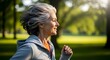 © Emon - Senior woman with gray hair jogging in a park during a sunny day, enjoying her outdoor activity