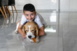 © Inna - A young boy smiles while resting on a tiled floor beside his beagle. The dog focuses on chewing a tasty treat, showcasing their friendship in a cozy home setting.