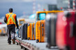 © NikonLamp - Airport baggage handler in safety vest is transporting luggage on conveyor belt, showcasing efficient airport operations and vibrant suitcase colors