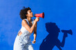 © VISTA by Westend61 - Woman with curly afro shouting into red megaphone against blue wall