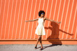 © VISTA by Westend61 - Happy woman with afro hairstyle in yellow dress dancing by orange wall