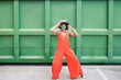 © VISTA by Westend61 - Smiling woman in red jumpsuit dancing outdoors by green wall