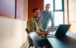 © Jacob Lund - Two mid-adult men laughing and working together at a desk with a laptop