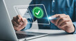 © HADI INCREDIBLE - Person using a laptop and touching a digital screen displaying document and verification check mark icons, representing compliance and approval.