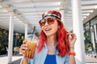 © EdNurg - Young woman with red hair and traditional central asian tubeteika hat enjoying an iced coffee beverage outdoors in summer