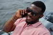 © TrueFrame Collective - Portrait of young adult Black man smiling while talking on smartphone outdoors near water, wearing sunglasses, showing relaxed facial expression and enjoying leisure time