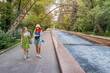 © EdNurg - Two young women enjoying a summer day in Almaty, Kazakhstan, walking and chatting beside a long fountain in a vibrant park filled with lush greenery
