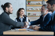 © opolja - Happy businessmen shaking hands at group board meeting